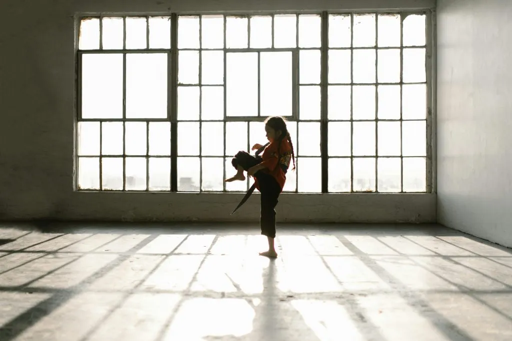Silhouette of a girl practising a kick in an empty sunlit studio