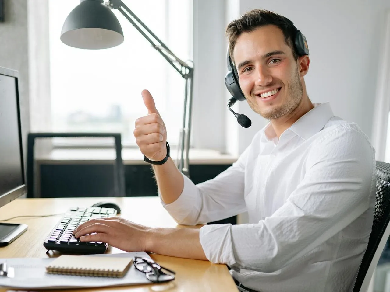 Smiling customer service agent in a headset giving a thumbs up at his desk