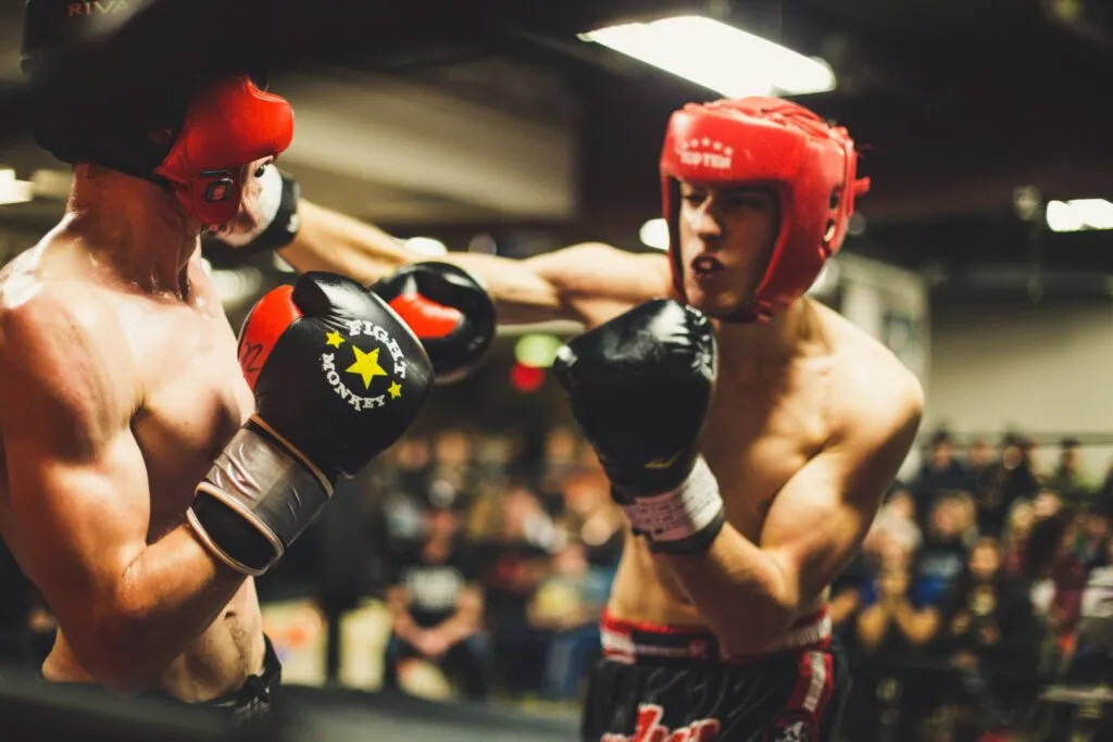 Two boxers in red headgear exchanging punches in front of a crowd