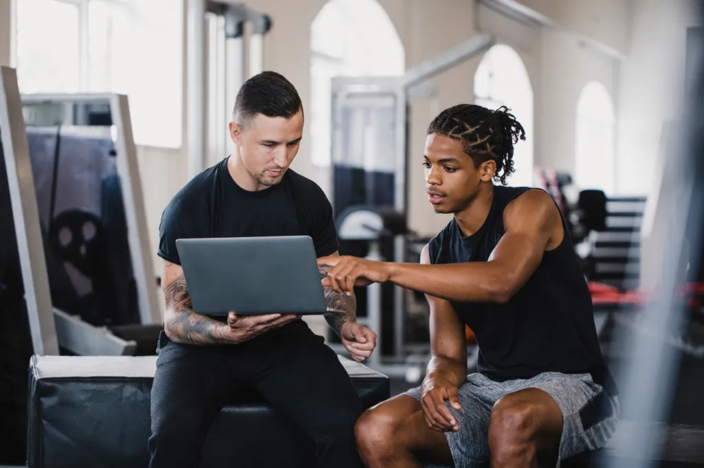 Trainer and athlete reviewing something together on a laptop in a gym