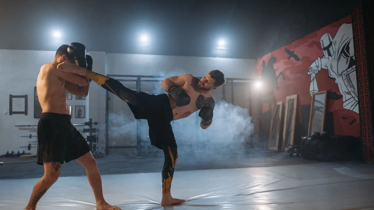 Kickboxer landing a body kick on an opponent in a smoky gym