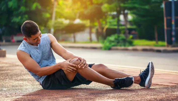 Runner sitting on the roadside holding an injured knee
