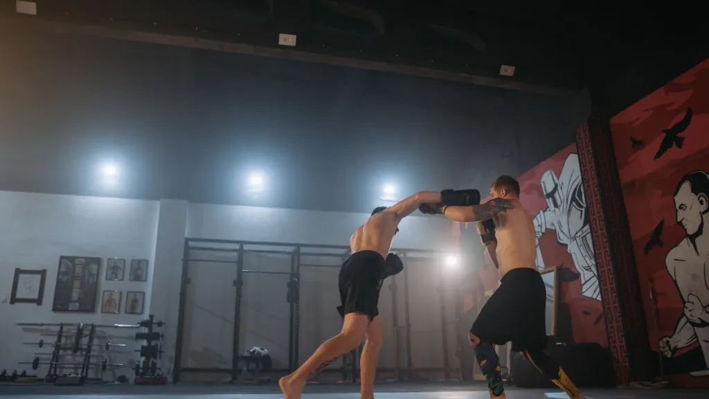 Two kickboxers sparring in a gym with a red mural on the wall behind them