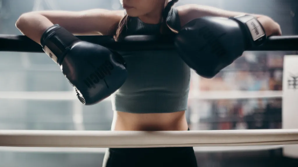 Boxer in gloves resting her arms on the ropes of a ring