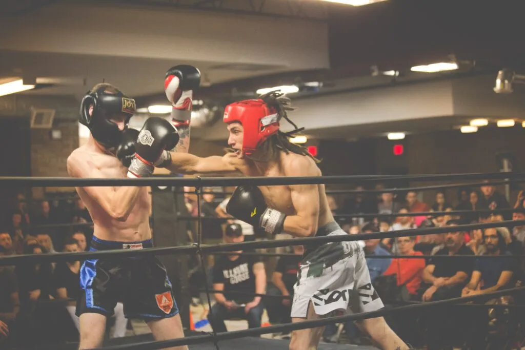 Two amateur kickboxers in headgear exchanging punches in a ring in front of a crowd