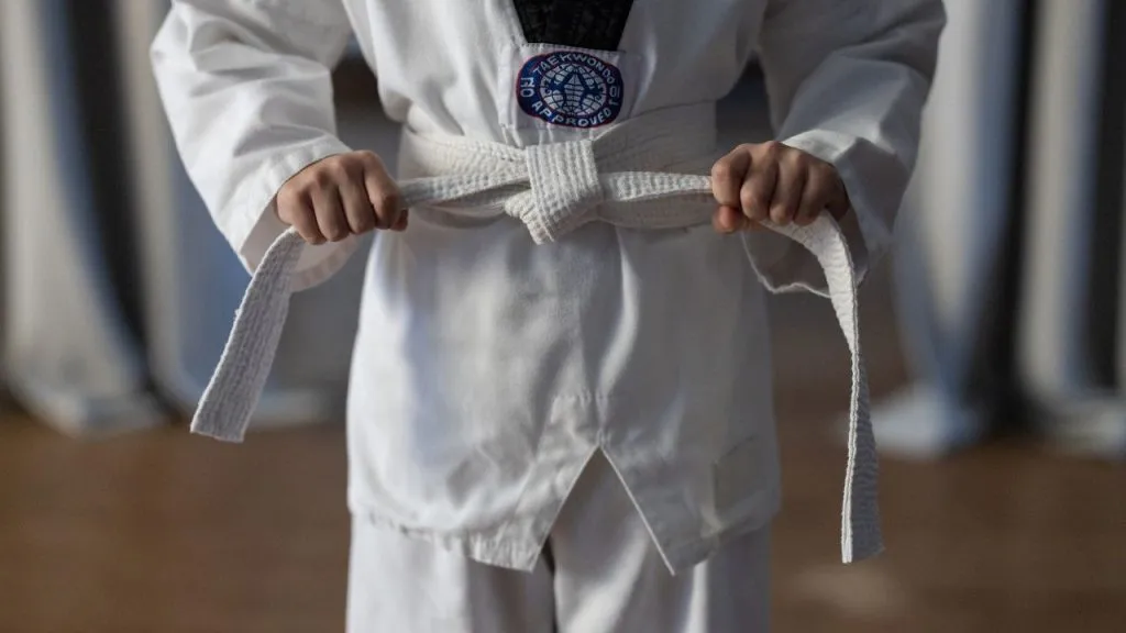 Close-up of a taekwondo student tying a white belt on a dobok