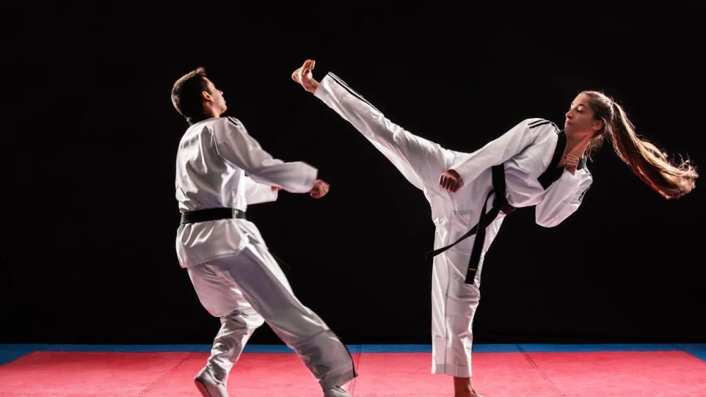 Two taekwondo athletes sparring, one landing a high kick to the head