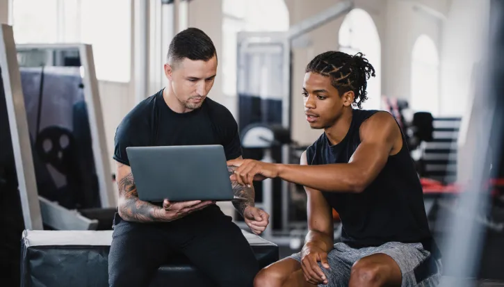 Trainer and athlete reviewing something together on a laptop in a gym