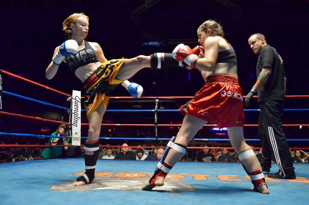 Two female kickboxers exchanging kicks in a ring at a fight night