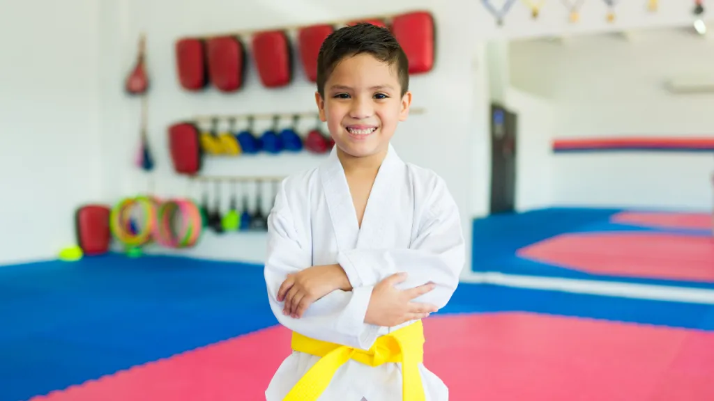 Smiling boy in a white gi and yellow belt with arms folded in a dojo