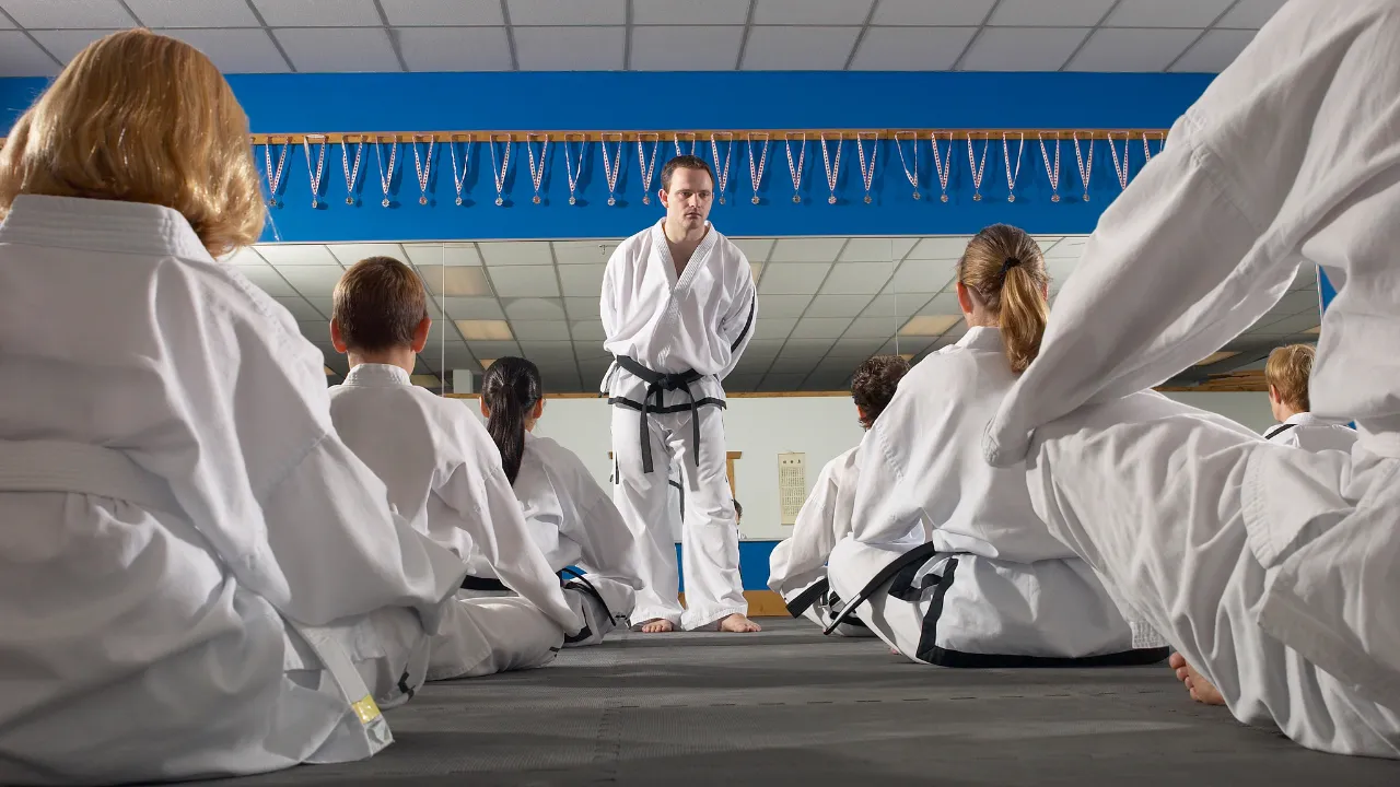 Martial arts instructor addressing students seated on the mat in a dojo